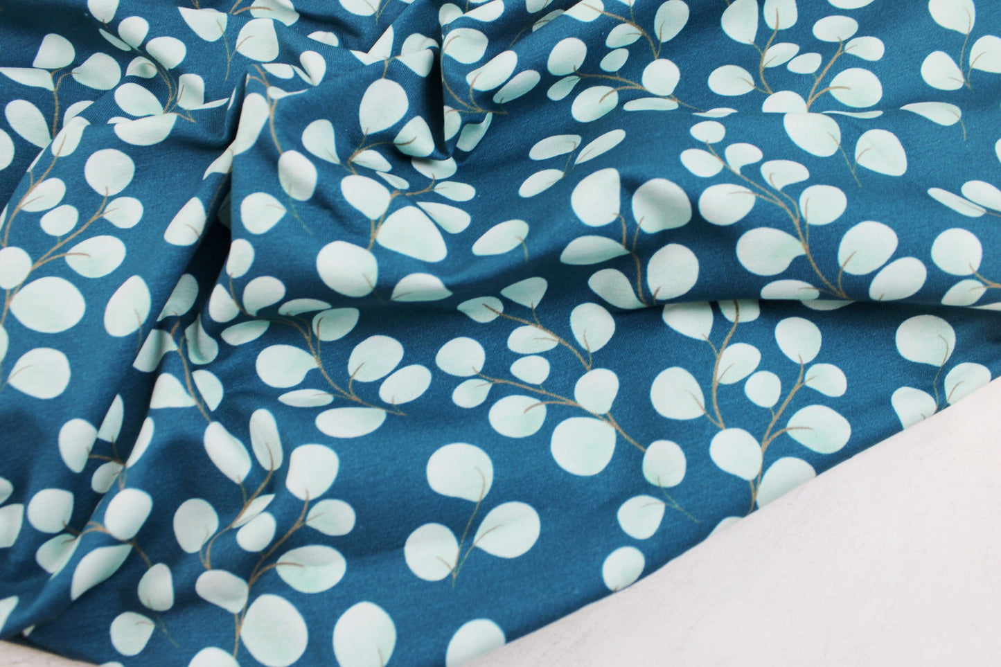 Baumwolljersey Fine Eukalyptus mit kleinen mintfarbenen Blättern auf petrol Grund