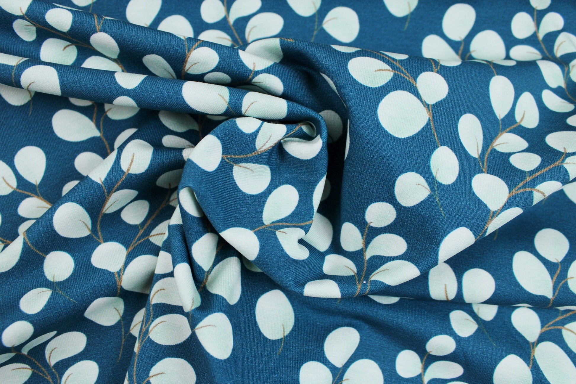 Baumwolljersey Fine Eukalyptus mit kleinen mintfarbenen Blättern auf petrol Grund gedreht