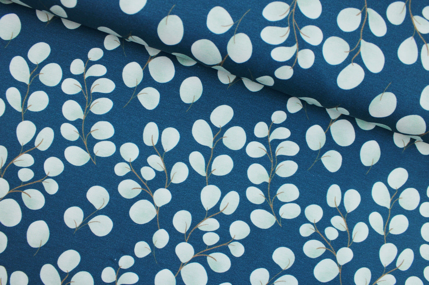 Baumwolljersey Fine Eukalyptus mit kleinen mintfarbenen Blättern auf petrol Grund quer