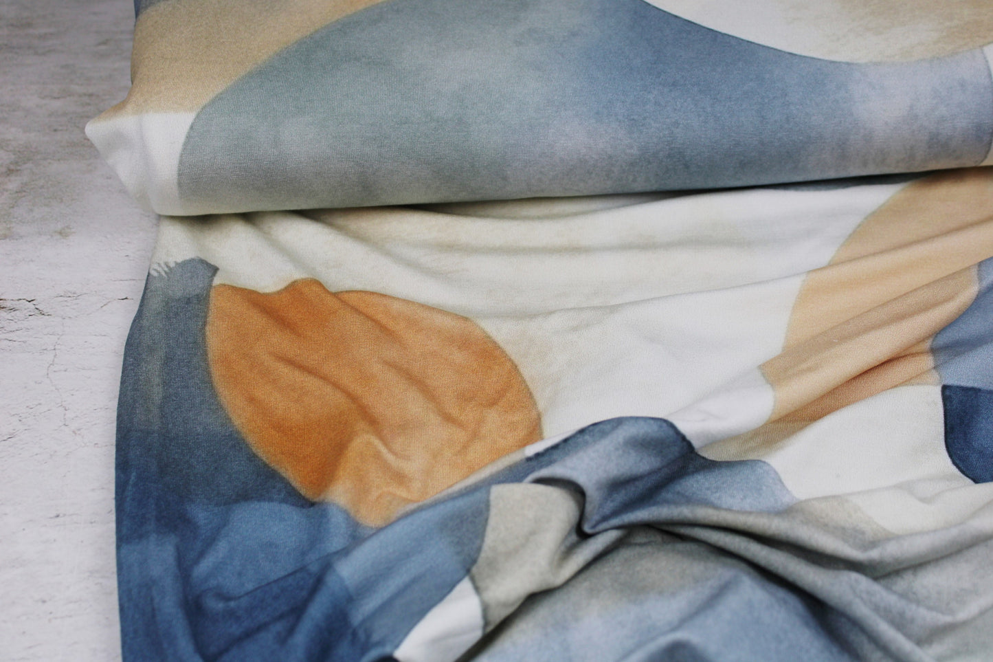 Viskosejersey mit großen geometrischen Formen in Blau und Rost auf hellem Grund Ballenansicht